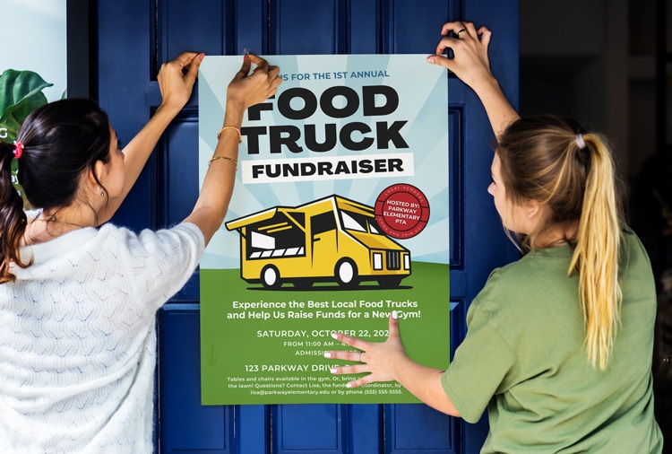 two women hanging a large food truck fundraiser poster onto a blue door with tape