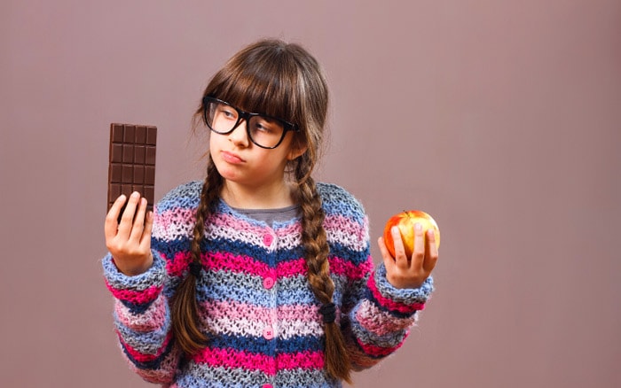 girl holding chocolate in one hand and an apple in the other signifying "would you rather" questions kids can answer