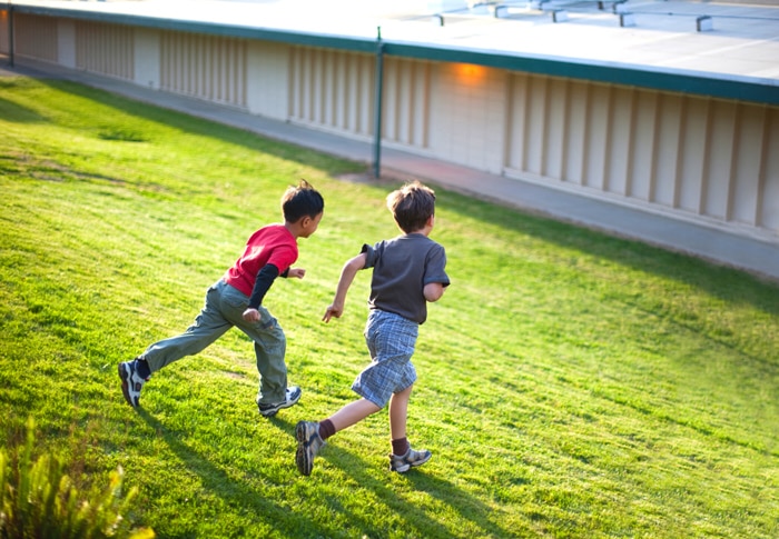 two elementary school boys running in field next to school building signifying a back to school scavenger hunt
