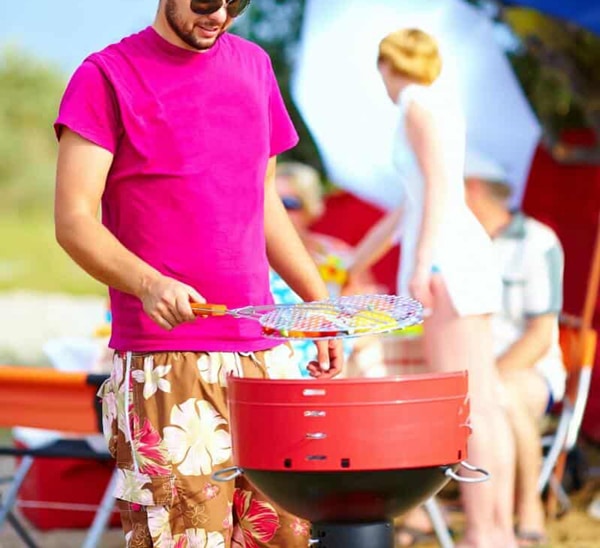 man grilling on a red grill with party in background signifying a back to school tailgate event