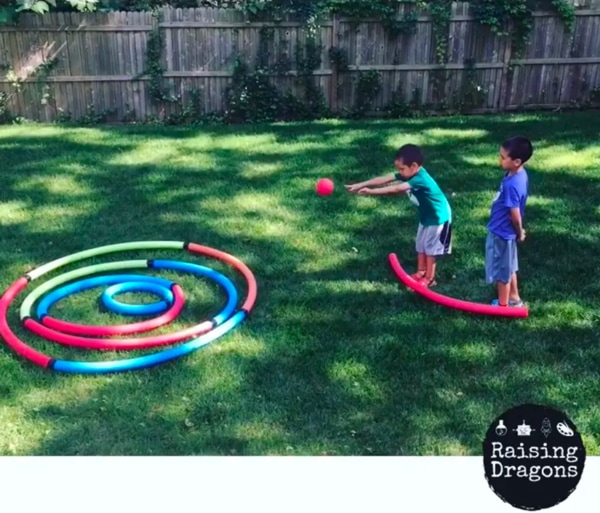 two boys playing an outdoor game made with pool noodles