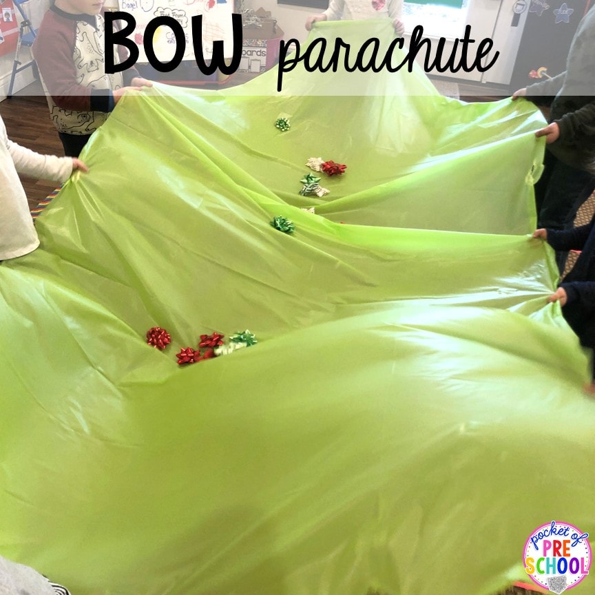 Children holding the edges of a green tablecloth with Christmas gift bows in the middle playing a game of bow parachute at their class Christmas party