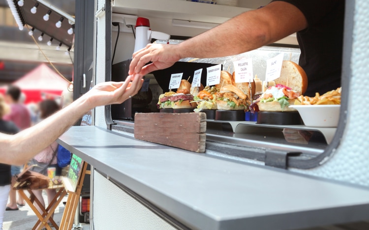 close up of food truck vendor handing change to customer with food samples displayed in the food truck window